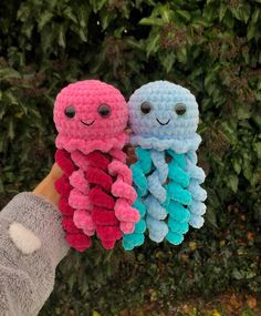 two small stuffed animals are being held by someone's hand in front of some bushes