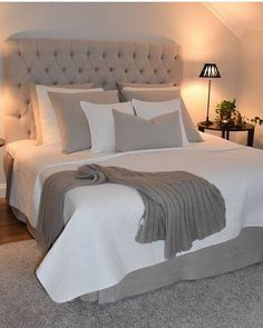 a bed with white sheets and pillows in a bedroom next to two lamps on either side of the bed