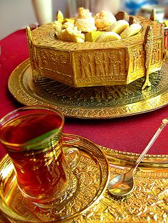 a table topped with gold plates filled with desserts and tea cups next to each other