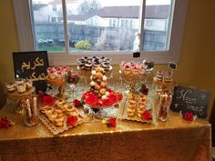 a table topped with lots of desserts and cupcakes next to a window