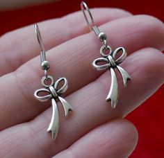 "Antique silver tone small bow knot charm earrings. Small bow charms dangling from stainless steel earring hooks. Earring length: 38mm; 1.5\" (including the earring hook) Earring hook material: stainless steel Charm material: Zinc alloy, Nickel safe, Lead free This listing is for one pair of bow earrings with rubber backs. This earring will come in a gift bag. I offer combined shipping costs which give you a shipping discount for ordering multiple items from my shop. Earrings care: Take them off Metal Bow Earrings For Gifts, Dangle Bow Earrings For Gift, Silver French Hook Earrings As Gift, Dangle Bow Jewelry As Gift, Silver Earrings With French Hook For Gift, Dangle Bow Jewelry For Gifts, Silver Bow Dangle Jewelry, Silver Dangle Earrings With Bow, Silver Dangle Jewelry With Bow Detail