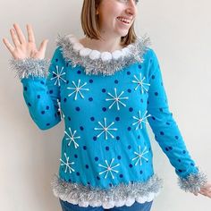 a woman wearing a blue sweater with snowflakes on it and holding her hands out