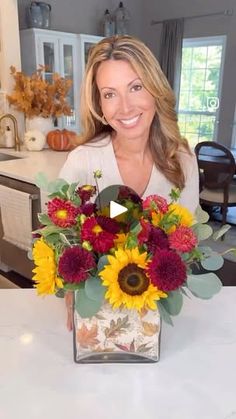 a woman sitting at a table with a vase filled with sunflowers and other flowers