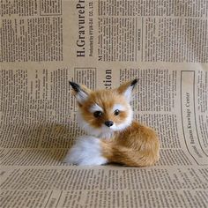 a small stuffed fox sitting on top of a newspaper