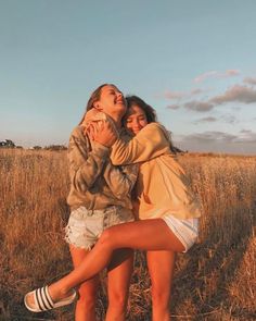 two young women are hugging in a field