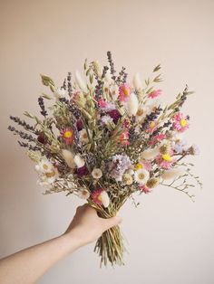 a hand holding a bouquet of flowers in front of a white wall with pink, yellow and purple colors