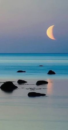 the moon is setting over the ocean with rocks