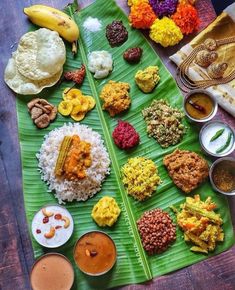 a large banana leaf covered in different types of food on top of a wooden table