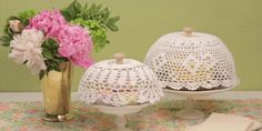 two white cakes sitting on top of a table next to vases filled with flowers