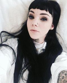 a woman with long black hair laying on top of a bed