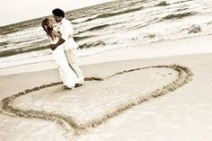 a man and woman are standing on the beach with a heart drawn in the sand