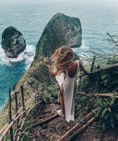 a woman standing on top of a hill next to the ocean with her back to the camera