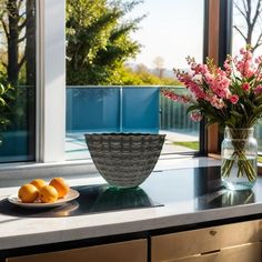 flowers and fruit are sitting on the counter in front of a large window with glass doors