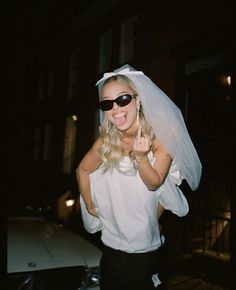 a woman wearing sunglasses and a veil on her head is standing in front of a car