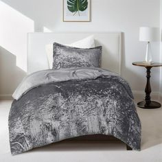 a bed with a white headboard and grey comforter in a room next to a lamp