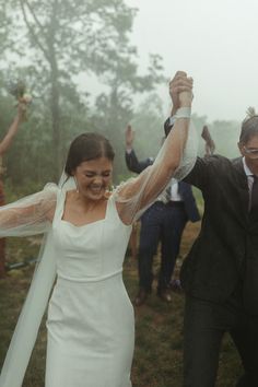 a bride and groom are dancing in the rain with their arms up to each other