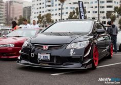 some cars are parked in a parking lot with people standing around them and one car has red rims on it