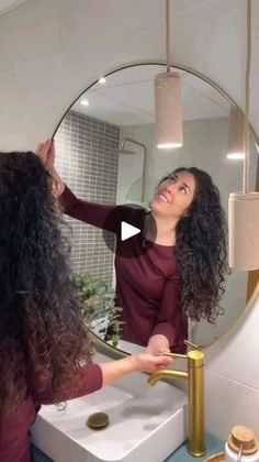 a woman standing in front of a mirror brushing her long dark hair with a brush