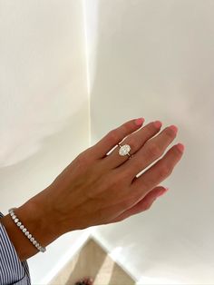 a woman's hand with a diamond ring on her left wrist and a white wall in the background