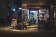 a store front at night with lights on the windows and plants in pots sitting outside