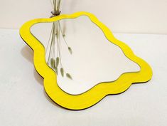 a yellow mirror sitting on top of a white table next to a vase filled with flowers