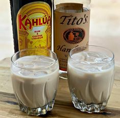 two glasses filled with white liquid next to a bottle of liquor and a glass full of ice cream