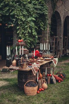 an outdoor table with candles, fruit and other food items on it in the grass