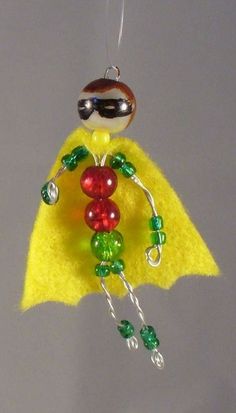 a glass ornament with a yellow cape and green beads hanging from it's side