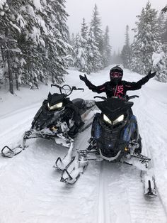 two people on snowmobiles in the middle of a snowy trail with their arms outstretched