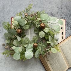 an open book sitting on top of a table next to a wreath with leaves and acorns