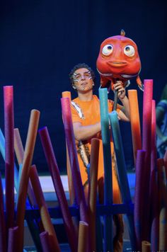 a man in an orange shirt is holding a red object with two eyes on it