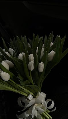 a bouquet of white tulips and green leaves on a black background with ribbon