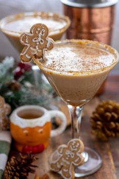 two glasses filled with drinks and decorated cookies on top of a wooden table next to pine cones