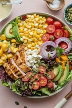 a salad with chicken, avocado, tomatoes, corn and other vegetables on it