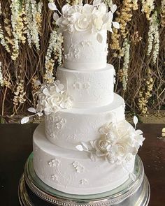 a three tiered white wedding cake with flowers on the top and bottom, sitting on a platter