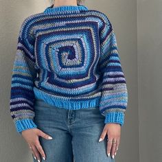 a woman standing in front of a wall with her hands on her hips wearing a blue and purple sweater