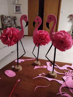 three pink flamingos standing on top of a wooden floor covered in paper mache