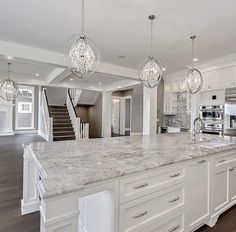 a large kitchen with marble counter tops and white cabinets, along with two chandeliers hanging from the ceiling