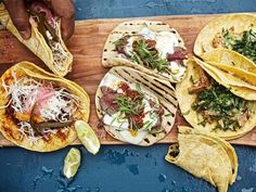 several tacos are laid out on a cutting board with limes and other toppings