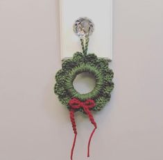 a green crocheted wreath hanging on a white wall with a red ribbon around it