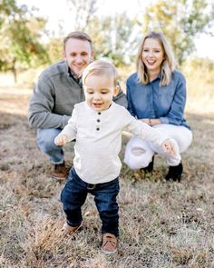 a man and woman kneeling down with a baby in front of them on the ground