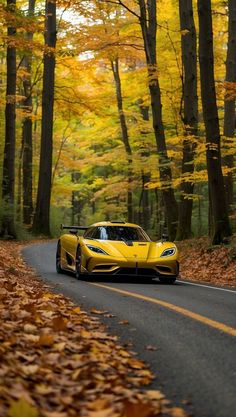 a yellow sports car driving down the road in front of trees with leaves on it