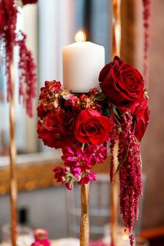 a candle and some red flowers in a vase on a table with candlesticks