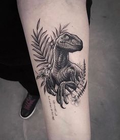 a black and white photo of a dinosaur tattoo on the left arm with fern leaves around it