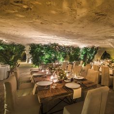 an indoor dining area with tables, chairs and greenery on the ceiling is lit by candles