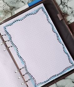 an open notebook sitting on top of a marble table next to a pen and paper