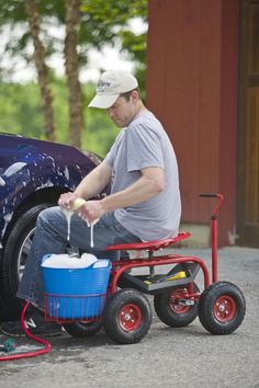 a man sitting on top of a red wagon next to a blue bucket filled with liquid