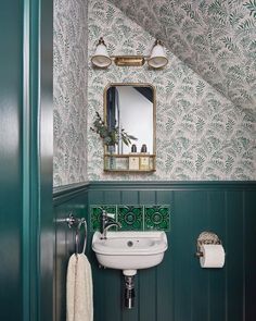 a bathroom with green and white wallpaper, a sink and mirror in the corner