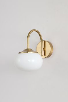 a wall light with a white glass ball on the side and an antique brass finish