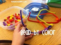 a child's hand is holding beads in front of a plastic container with scissors